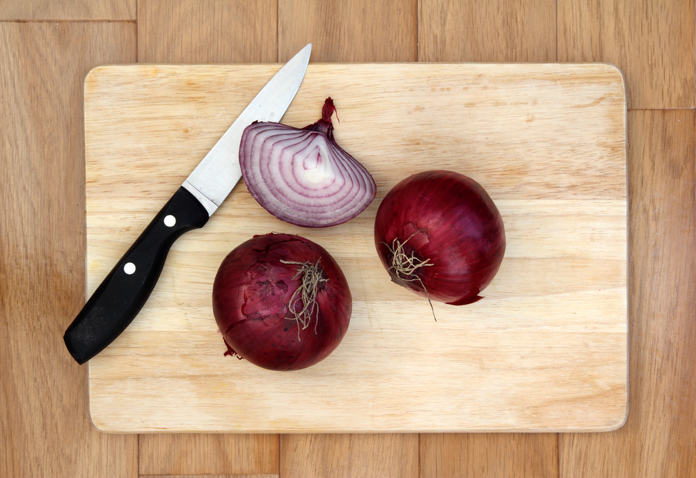 Red onions and knife on a wooden chopping board